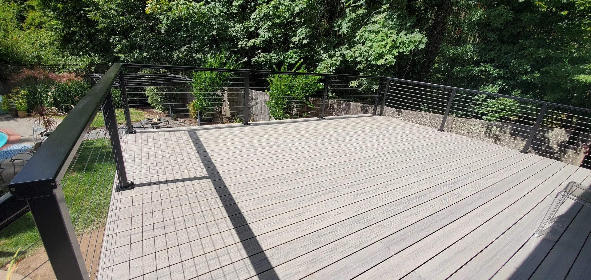 Wide gray composite deck overlooking a green backyard, with black posts and cable railing
