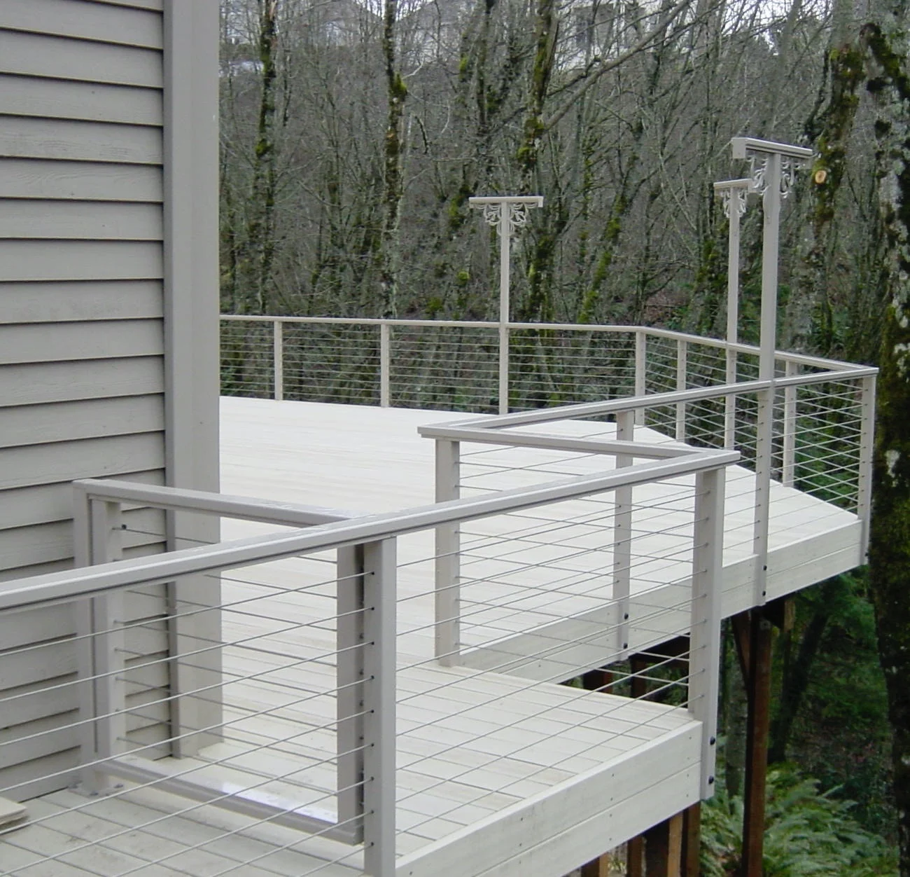 Light composite deck with pale cable railing overlooking a wooded slope